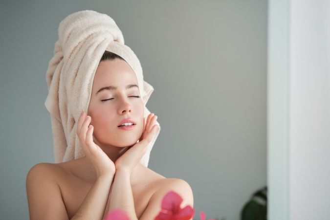 woman with eyes closed touching cheeks after shower