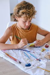 Serious boy painting stone at table