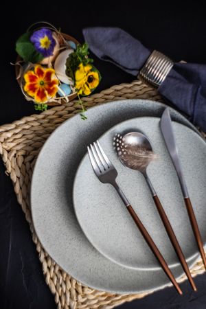 Easter table setting with elegant grey plates, colorful flowers and decorative feather