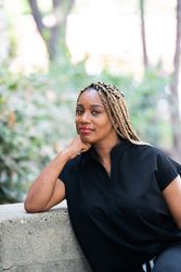 Portrait of a woman in black scrubs sitting outside with hand under her chin