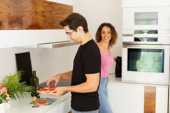 Happy adult man standing near cooking range with woman and arranging salad