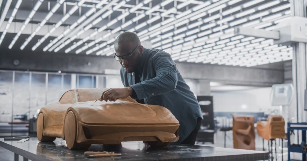 Black Designer Working on a New Prototype, Sculpting Industrial Plasticine Clay 3D Model of Sporty Coupe.