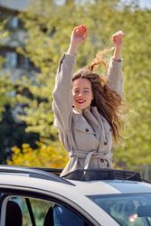 Excited woman standing with arms raised in car sunroof