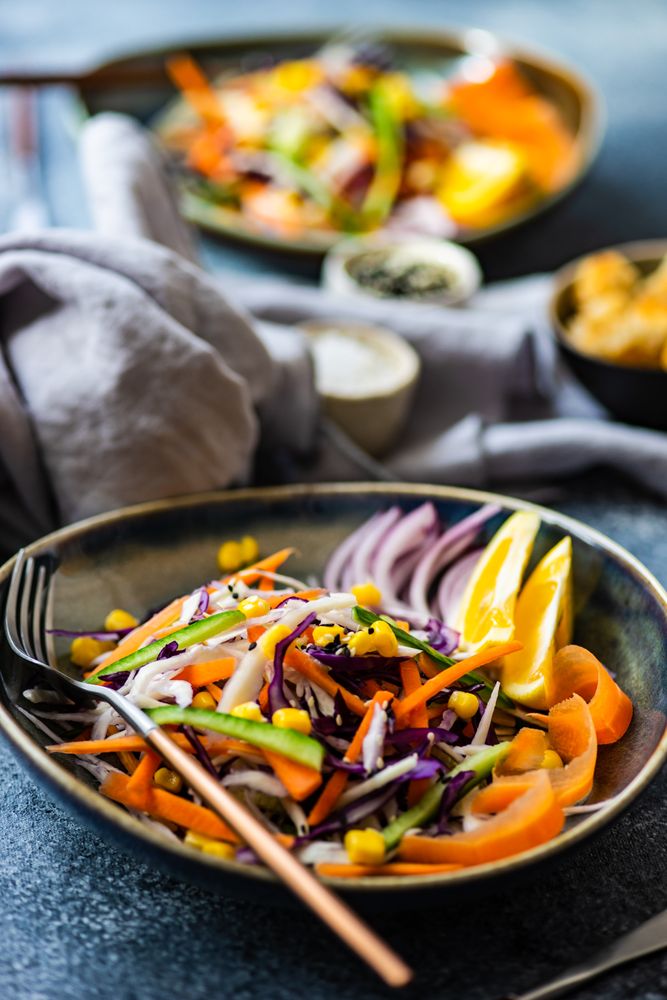 Healthy colorful vegetable salad and lemon slices in bowl on counter with copy space