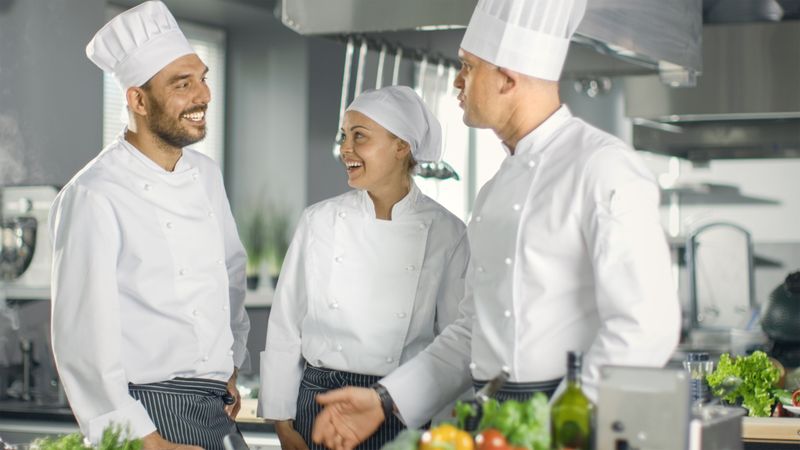In the Modern Kitchen Staff Member Have Discussion with Chef. Kitchen is Full of Food Ingredients, Vegetables, Meat, Boiling Soup.