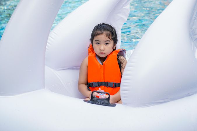 Girl in lifejacket sitting in large inflatable toy in pool