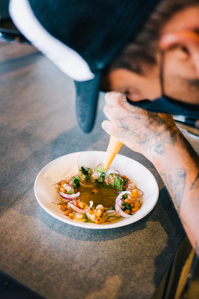 Tattooed chef piping sauce onto delicate dish