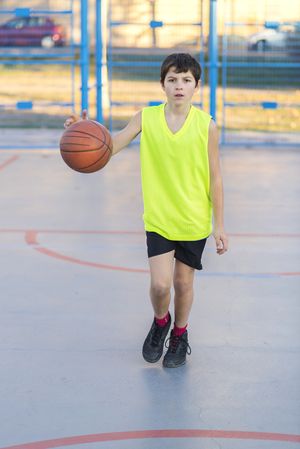 Cute boy in yellow shirt plays basketball on city playground