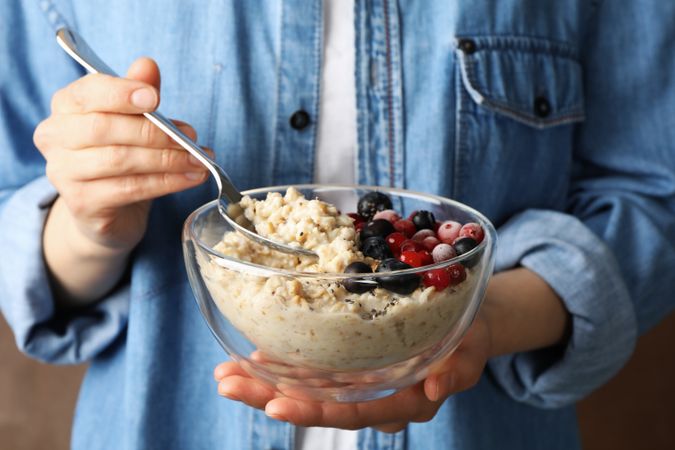 Woman holds bowl with oatmeal porridge with fruits. Close up
