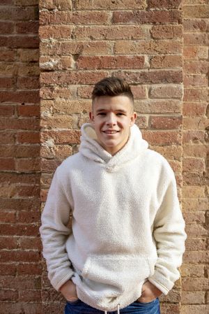 Portrait of young male with hands in pocket leaning against brick wall