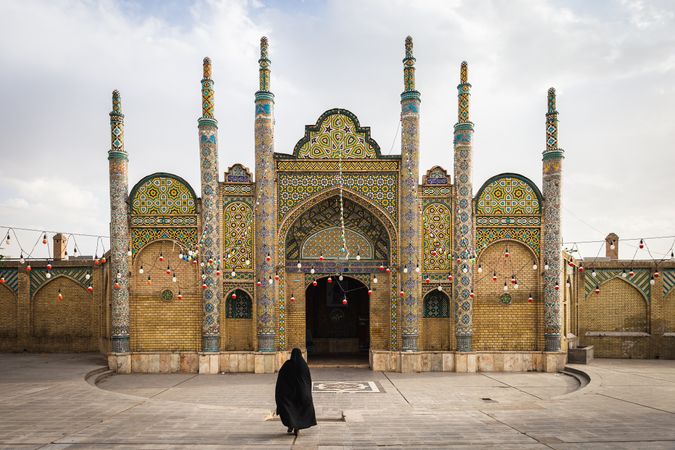 Back view of woman in dark thobe standing against Shahzadeh mosque in Qazvin, Iran