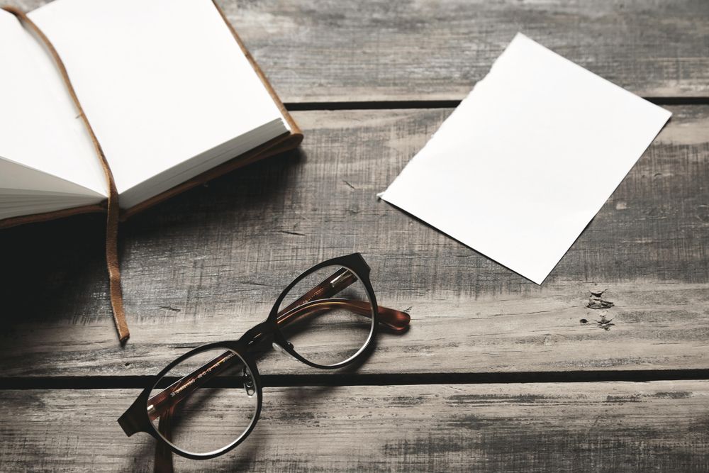 Notebook, paper and glasses on wooden table
