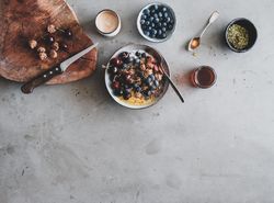 Oat granola yogurt bowl with cherries, blueberries, honey, nuts, coffee, wooden board