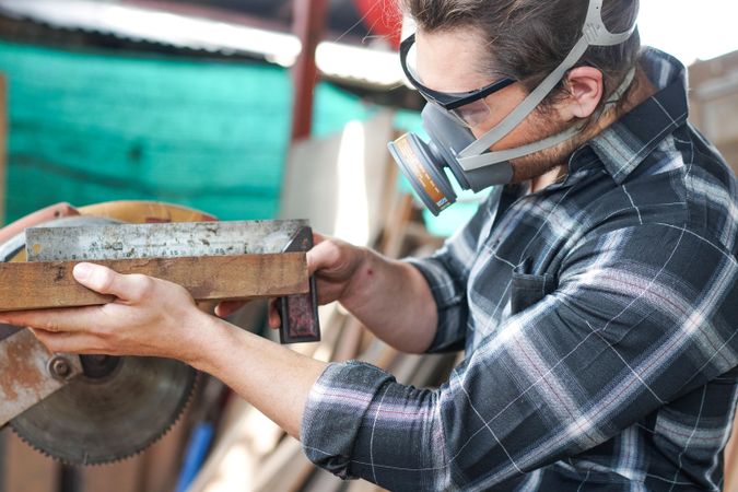 Carpenter in dust mask measuring wood in shop