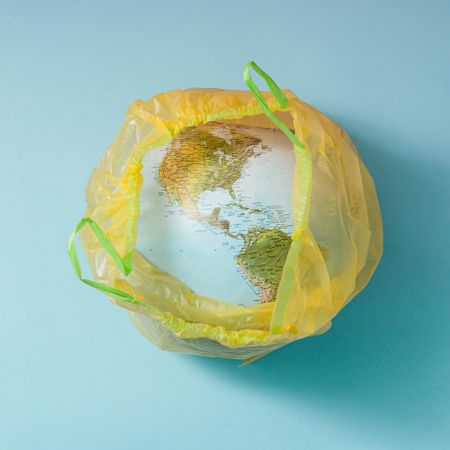 Earth in plastic yellow trash bag on blue background
