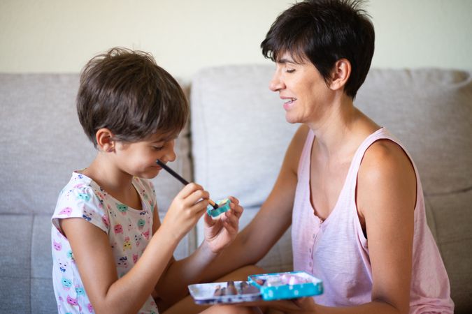 Little girl playing with make up brushes with her mother