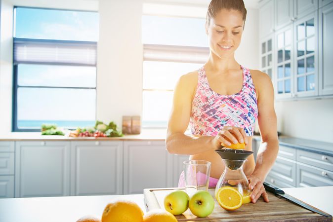 Athletic woman in sports bra juicing an orange