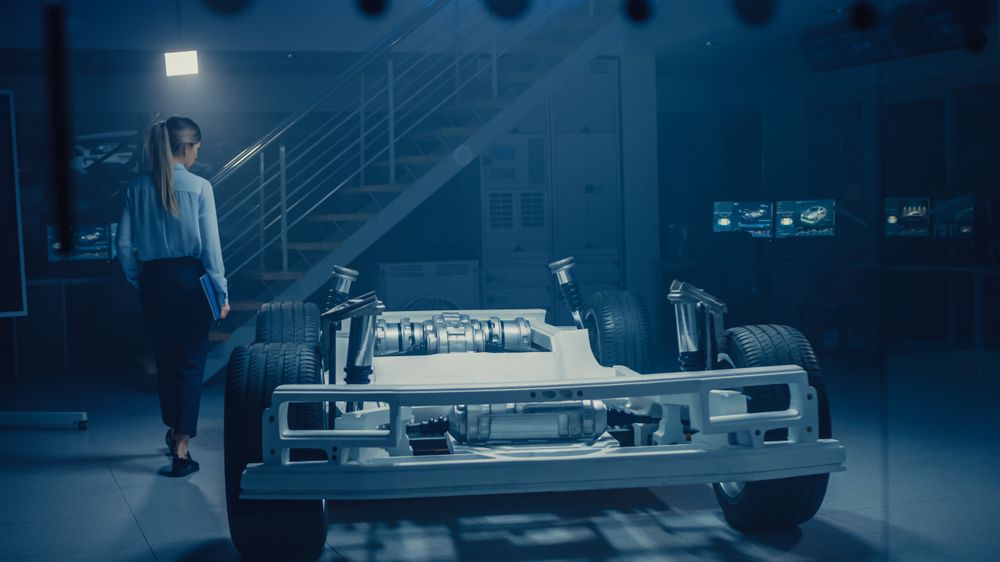Automobile Engineer Working on Electric Car Chassis Platform, Using Tablet Computer Augmented Reality with 3D CAD Software Modelling.