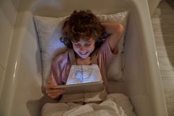 Cheerful child browsing tablet in bathtub
