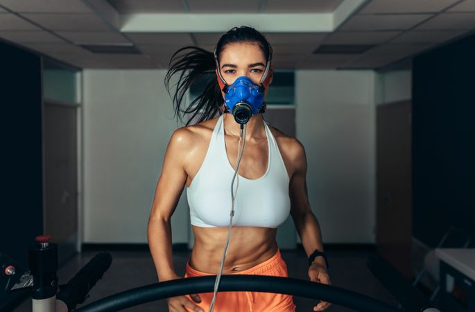 Portrait of female runner wearing mask on treadmill in sports science lab