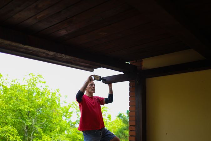 Older man installing a light on his home.