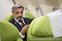 Man using smart phone with ear buds in flight 4MjGGb
