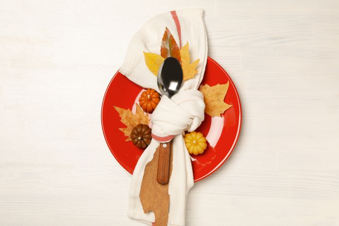 Spoon in towel on plate, leaves and pumpkins on light background, top view