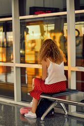 Stylish cheerful woman sitting on metal bench in glass hallway of airport in Texas