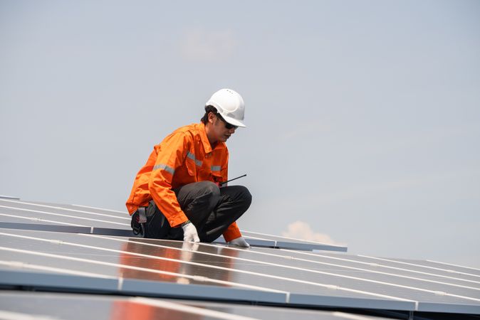 Male engineer checking solar cell  or photovoltaic cell by electronic device installed on the roof of the factory. Technician worker repair or inspect the system. Industrial renewable energy concept
