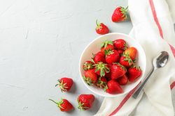 Plate with fresh strawberries, spoon and kitchen towel on bright background, top view and space for text