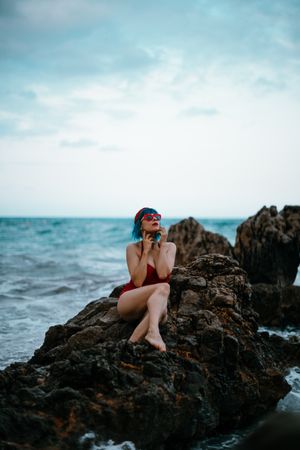 Graceful woman with trendy hairstyle tanning on rocky stone in water