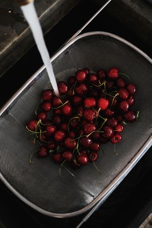 Cherries in strainer with running water over kitchen sink