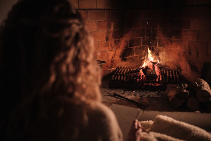 Crop female reading book near fireplace