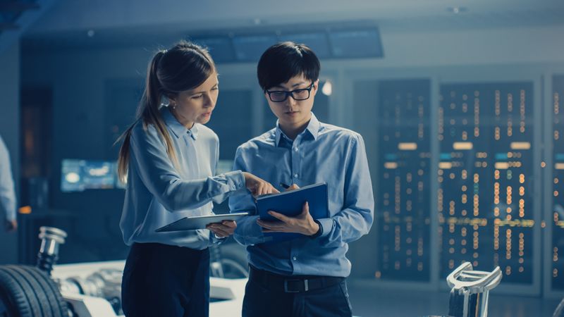 Male and Female Automobile Design Electric Car Engineers Having Conversation, Use Clipboard to Check Maintenance Issues.