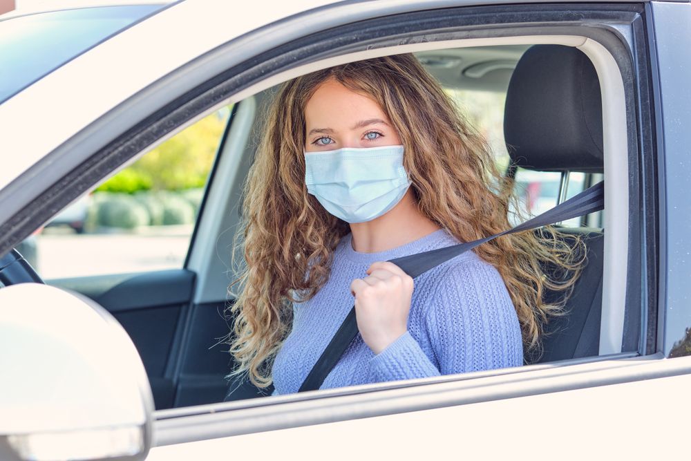 Young woman in mask sitting in car driver seat