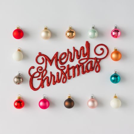 Border of colorful Christmas bauble decorations on light background with “Merry Christmas”