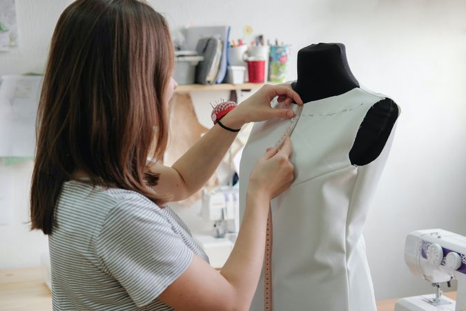 Seamstress holding measurement tape standing beside mannequin