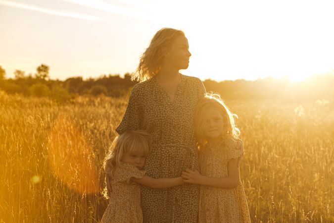 Little sisters hugging mother against bright sunset