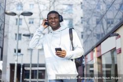 Young Black man standing in the street using headphones 56GRQY