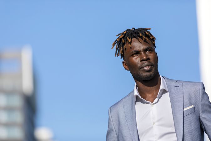 Black man wearing elegant clothes standing in the street while looking in the distance on sunny day