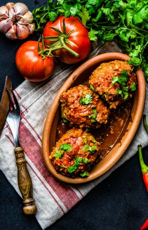 Three large meatballs served on table surrounded by fresh vegetables and herbs