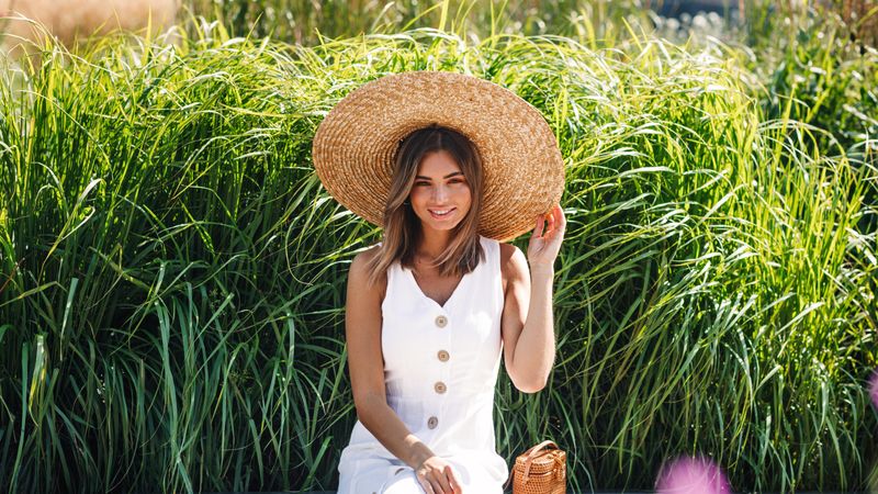 Happy woman sitting in front of long grass with straw hat