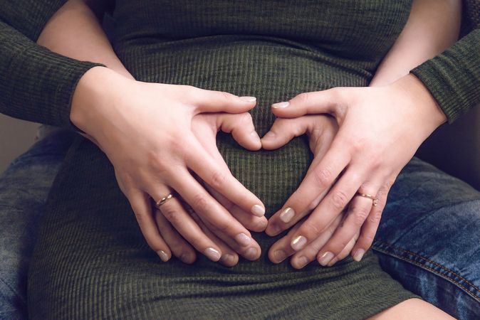 Heart shaped hands over a belly of pregnancy