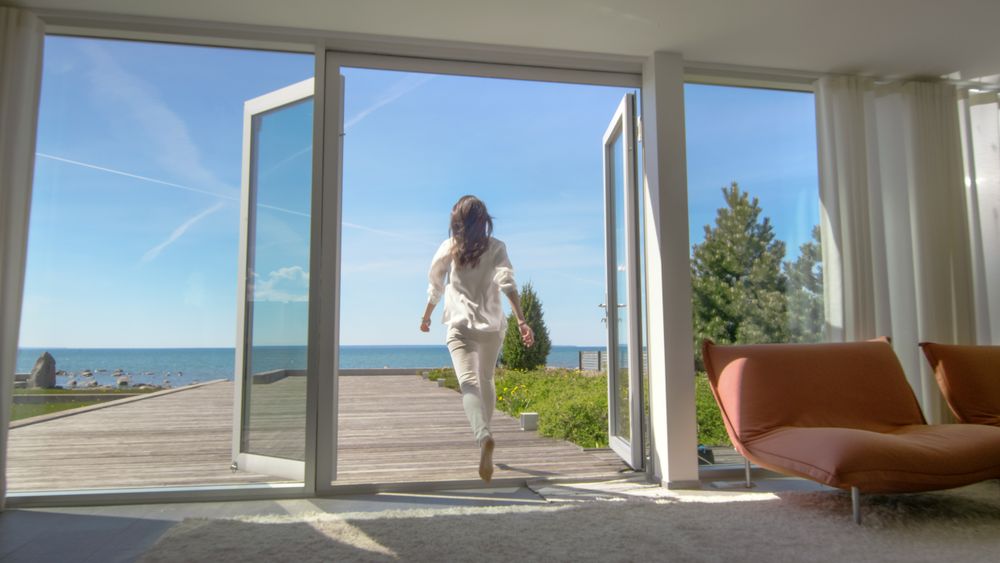 Shot of a Brunette with Loose Hair Opening Doors of the Balcony and Walking onto Sunny Terrace with Seaside View.