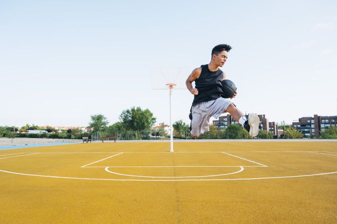 Young man playing on yellow basketball court outdoor jumping happily