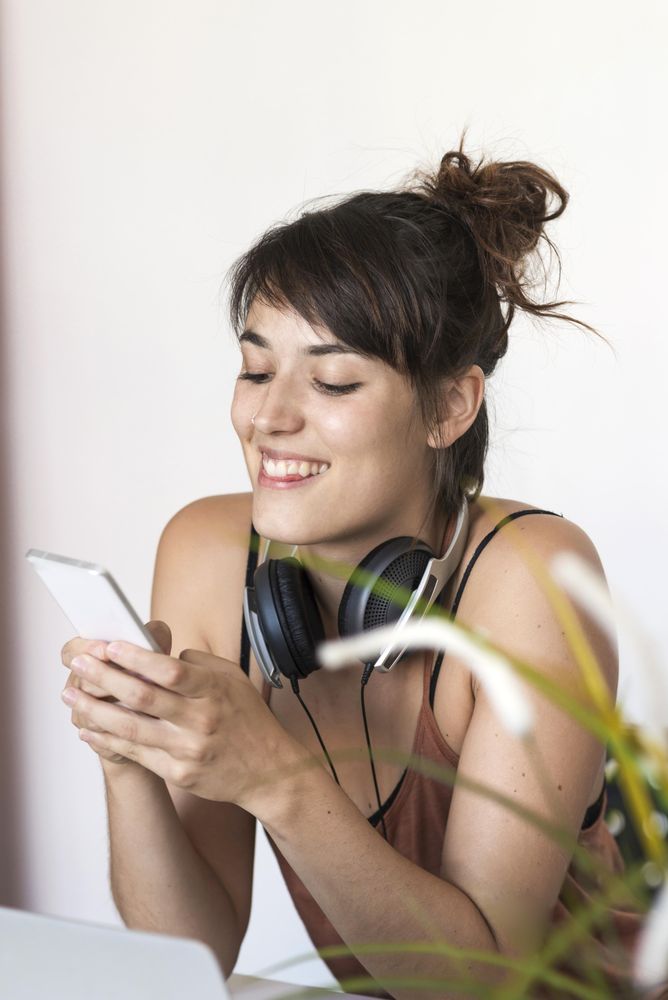 Happy female checking smartphone in front of laptop in home office