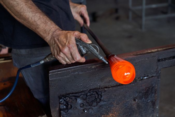Glassmith blowing on hot glass with air gun during work