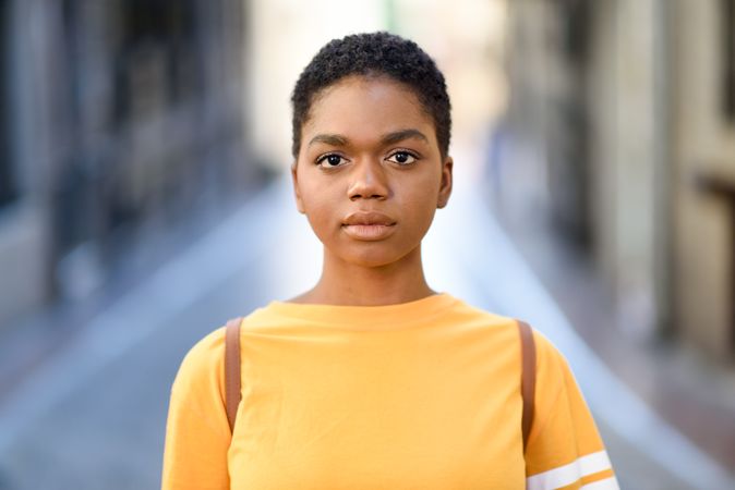 Female in yellow t-shirt looking at camera standing on street