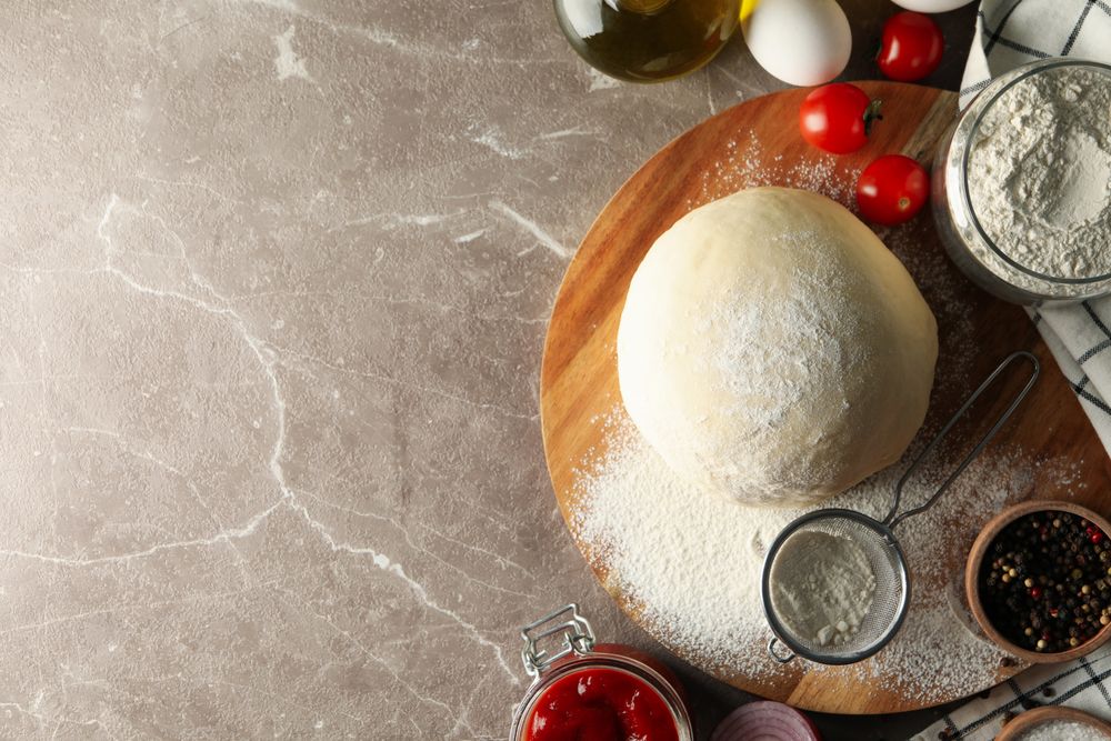 Dough and ingredients for cooking pizza on gray background