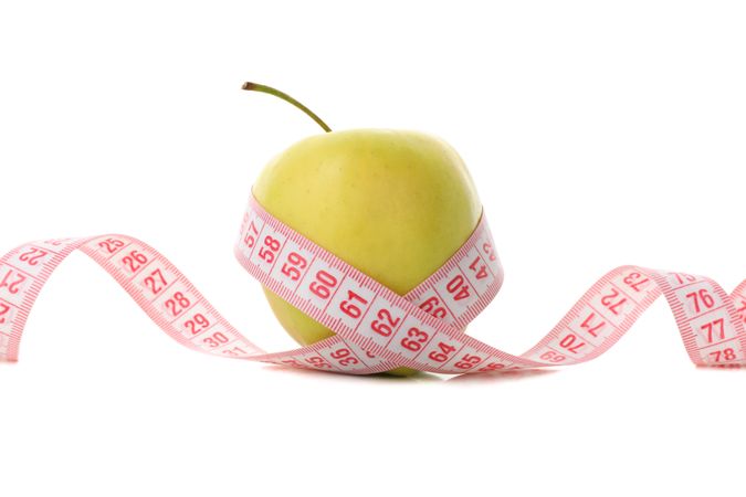 Measuring tape with apple isolated on light background